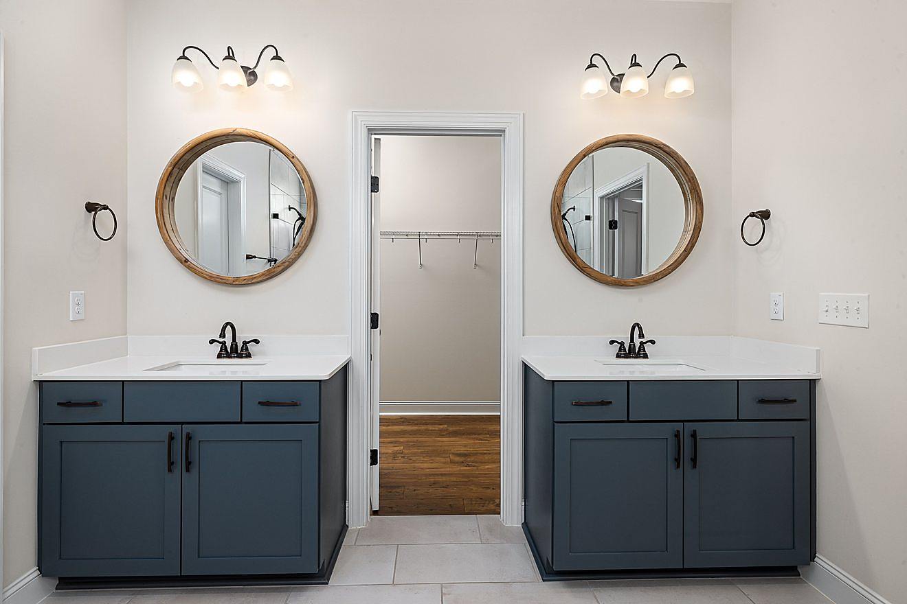 Finished bathroom with two dark blue vanities, round wood-framed mirrors, and a view into a connected walk-in closet