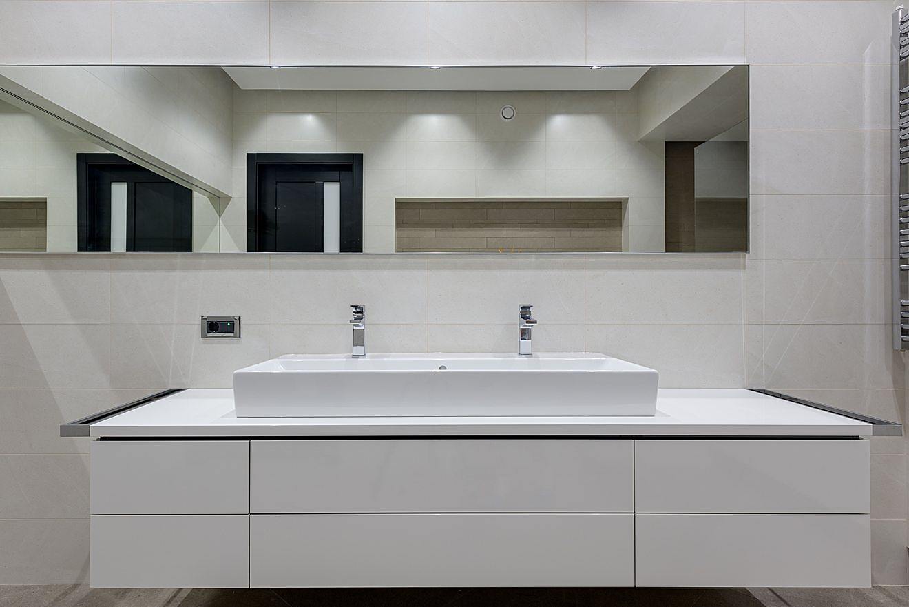 Modern bathroom vanity with a wide trough sink, dual faucets, and a full-width mirror