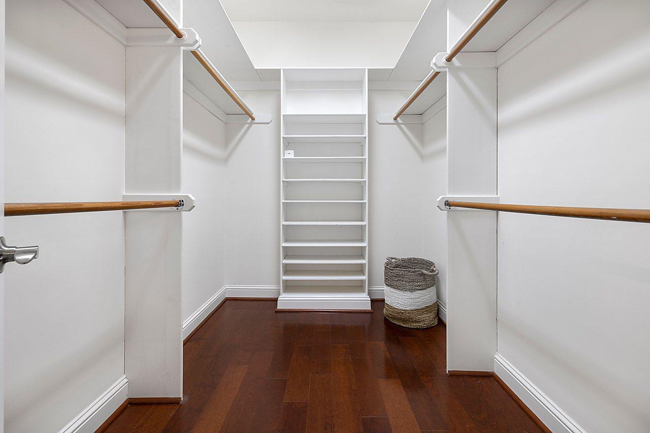 Custom walk-in closet with hanging rods on both sides, a center shelving tower, and hardwood flooring