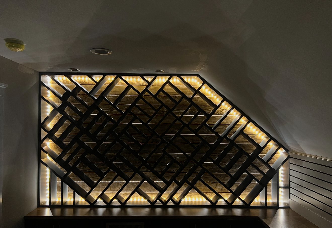 Custom geometric built-in display wall with warm LED lighting shown in the evening