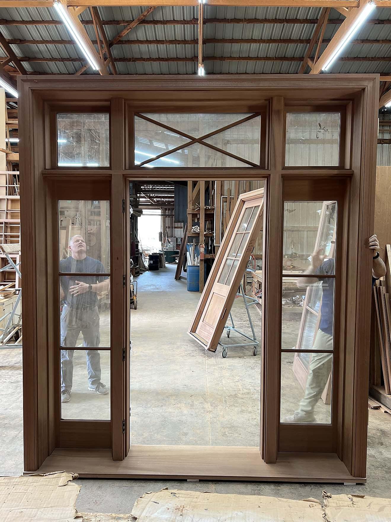 Custom wood window and door frame with an X-brace mullion pattern and transom lites, shown in the workshop