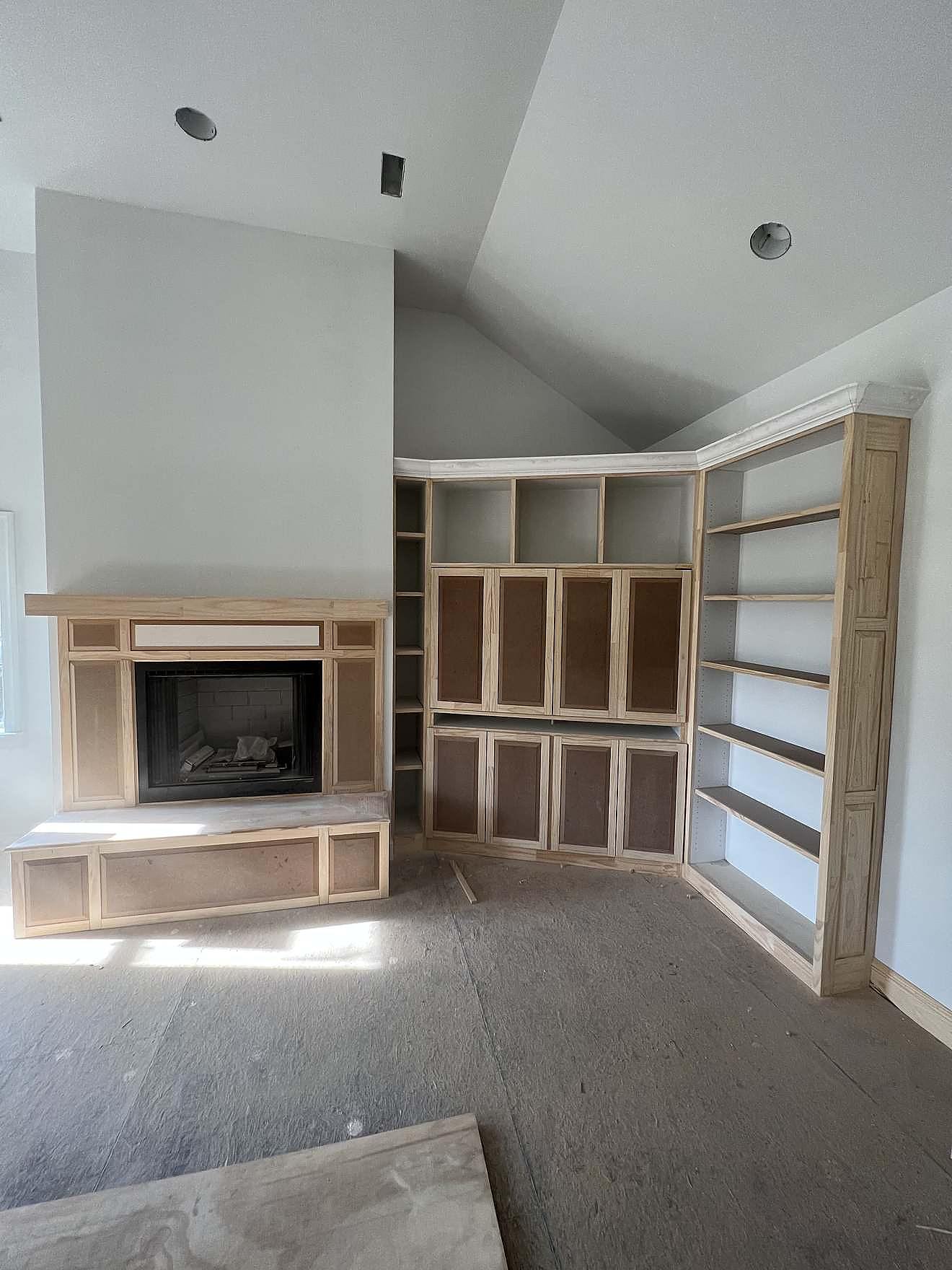 Custom fireplace surround and built-in shelving under construction in a vaulted great room