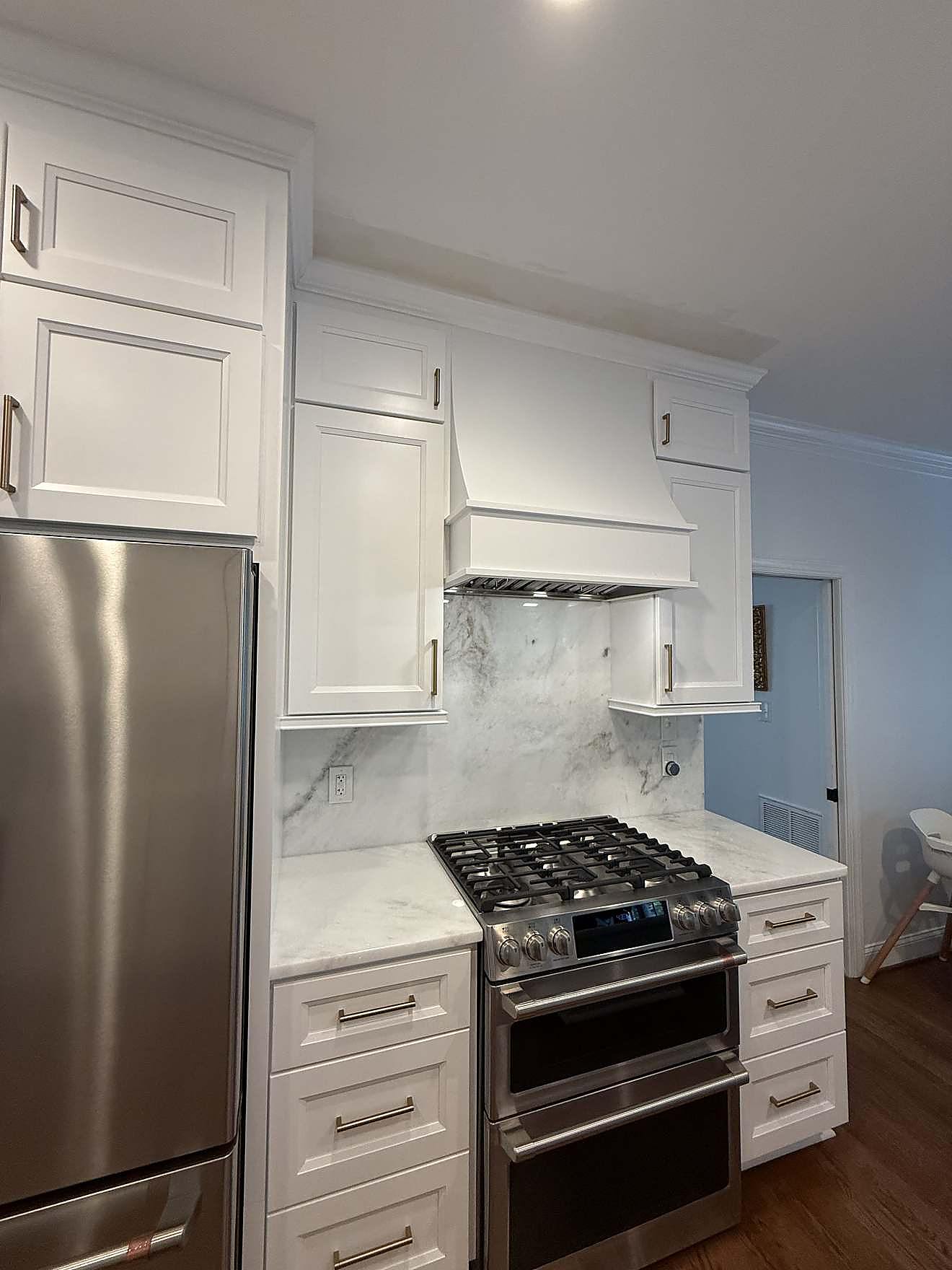 Finished kitchen range wall with white cabinetry, marble backsplash, and brass fixtures