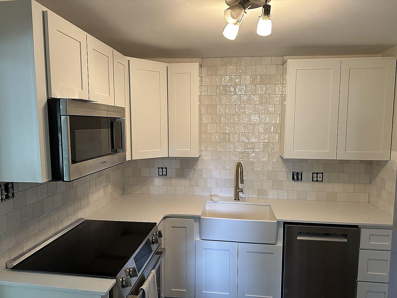 Finished kitchen installation with white shaker cabinetry, subway tile backsplash, and a farmhouse sink